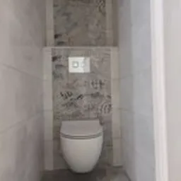 Kompakt WC podwieszany z przyciskiem spłukującym na tle szarej, wzorzystej płytki, obramowany białymi płytkami imitującymi marmur w małej łazience.