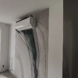 Ściana w pokoju z abstrakcyjnym wzorem przypominającym marmur, klimatyzator zamontowany na ścianie, panele podłogowe w odcieniach szarości.