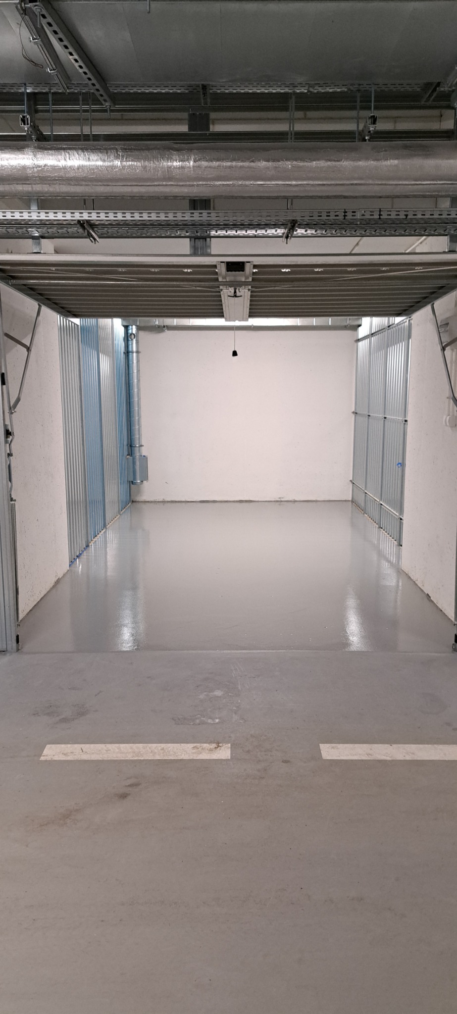 Puste, pomalowane na szaro pomieszczenie magazynowe z metalową konstrukcją sufitu i ścianami z blachy trapezowej, oświetlone pojedynczą żarówką.