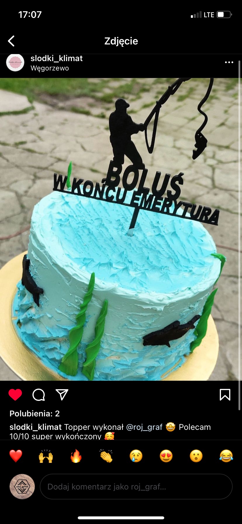 Tort urodzinowy z błękitnym kremem imitującym wodę, dekorowany czarnymi sylwetkami ryb, wodorostów i figurki wędkarza z napisem 'Boluś w końcu emerytura', umieszczony na złotym podkładzie.