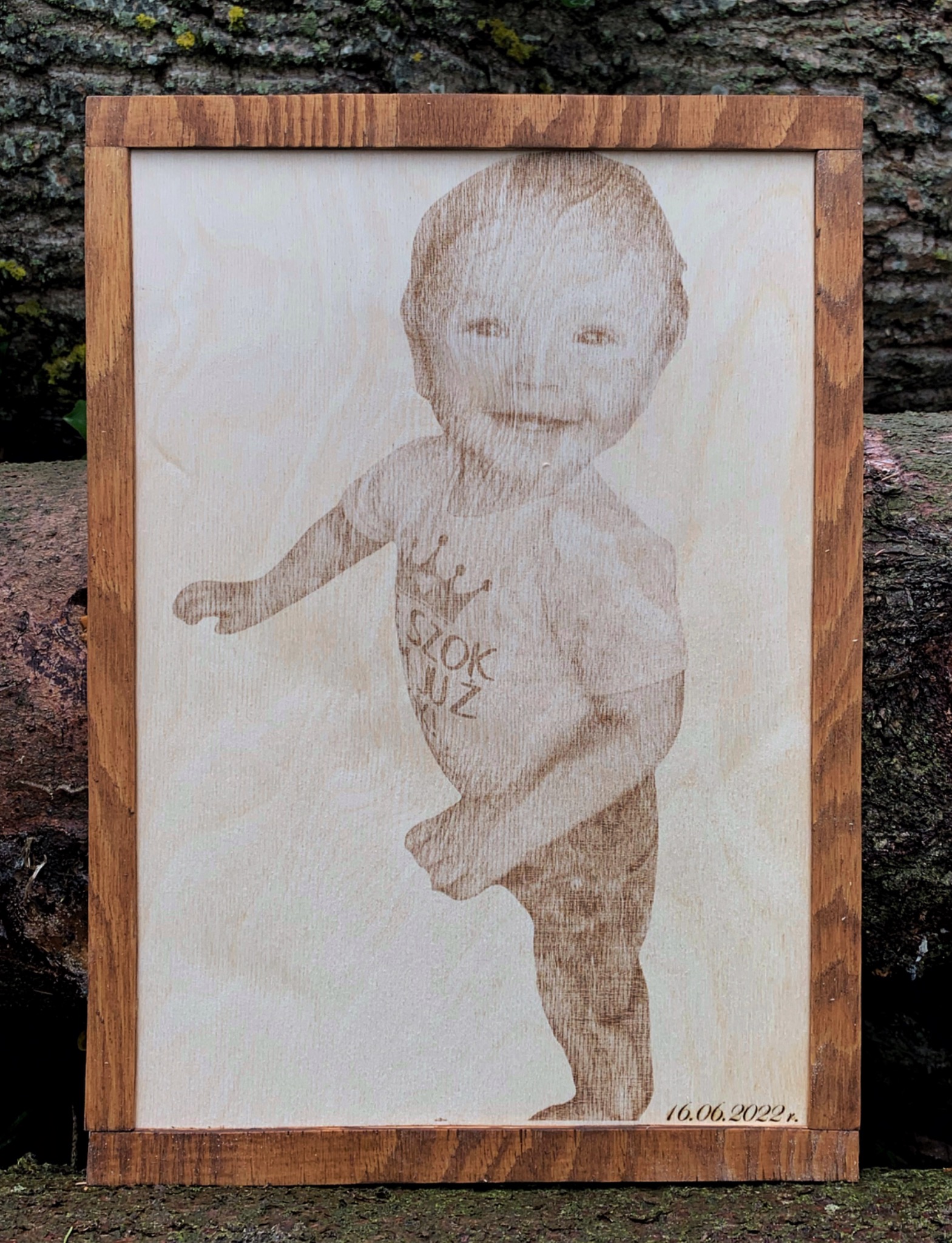 Portret dziecka wygrawerowany laserowo na jasnym drewnie w brązowej ramce, z datą 16.06.2022 w prawym dolnym rogu.