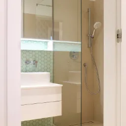 Nowoczesna łazienka z kabiną prysznicową typu walk-in, umywalką nablatową na szafce z szufladami i heksagonalnymi płytkami w odcieniach zieleni.