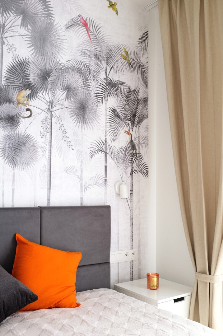 Sypialnia z tapetą w tropikalny las z motywami zwierzęcymi, szarą ramą łóżka, pomarańczową poduszką i beżowymi zasłonami.