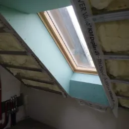 Poddasze w trakcie adaptacji: okno dachowe otoczone płytami gipsowo-kartonowymi, izolacja wełną mineralną w przestrzeni między krokwiami, widoczne profile metalowe i folia paroizolacyjna Isover...