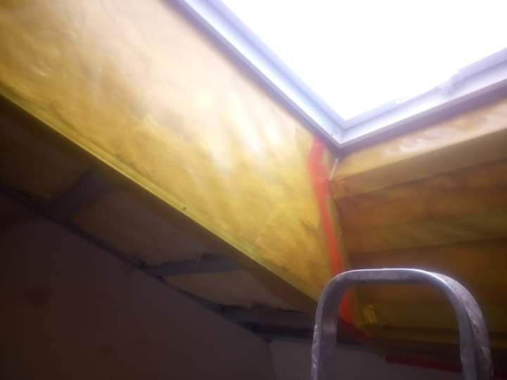 Poddasze z oknem dachowym w trakcie ocieplania, widoczna żółta wełna mineralna, fragment drabiny w dolnej części kadru.