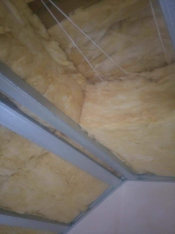 Ocieplenie poddasza wełną mineralną, widoczne metalowe profile konstrukcyjne sufitu podwieszanego i sznurki podtrzymujące izolację.