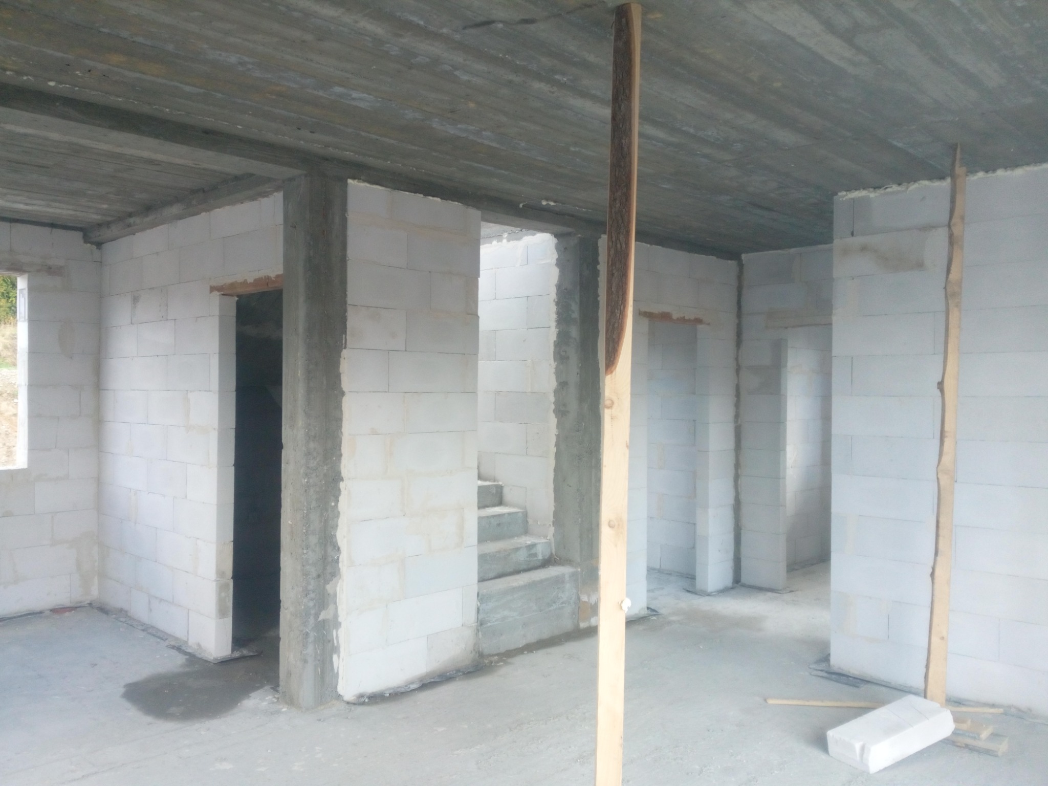 Wnętrze surowego domu w trakcie budowy: ściany z bloczków, betonowy strop, drewniana stempla podtrzymująca strop w pomieszczeniu ze schodami.