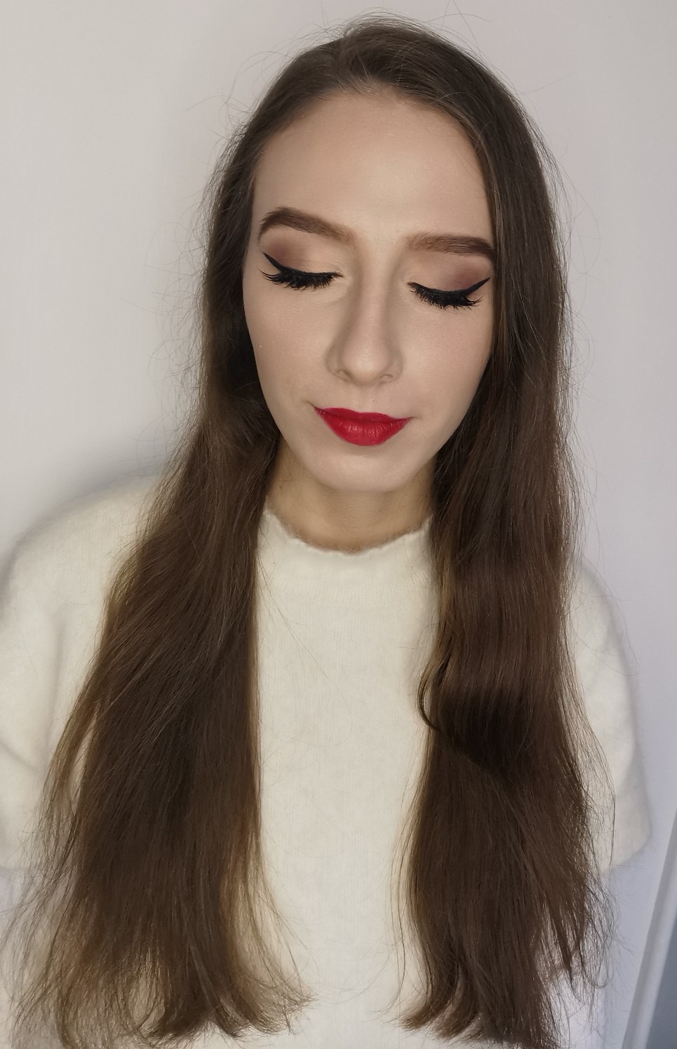 Portret kobiety z zamkniętymi oczami, prezentującej makijaż oczu z kreską i czerwonymi ustami. Uwagę zwraca intensywny kolor szminki i precyzyjnie wykonana kreska na powiece.