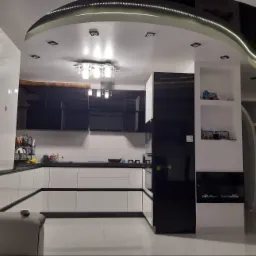 Nowoczesna kuchnia z białymi szafkami dolnymi i czarnymi górnymi, oświetlona lampą sufitową i listwą LED w suficie podwieszanym, z widocznym dużym zegarem na ścianie.