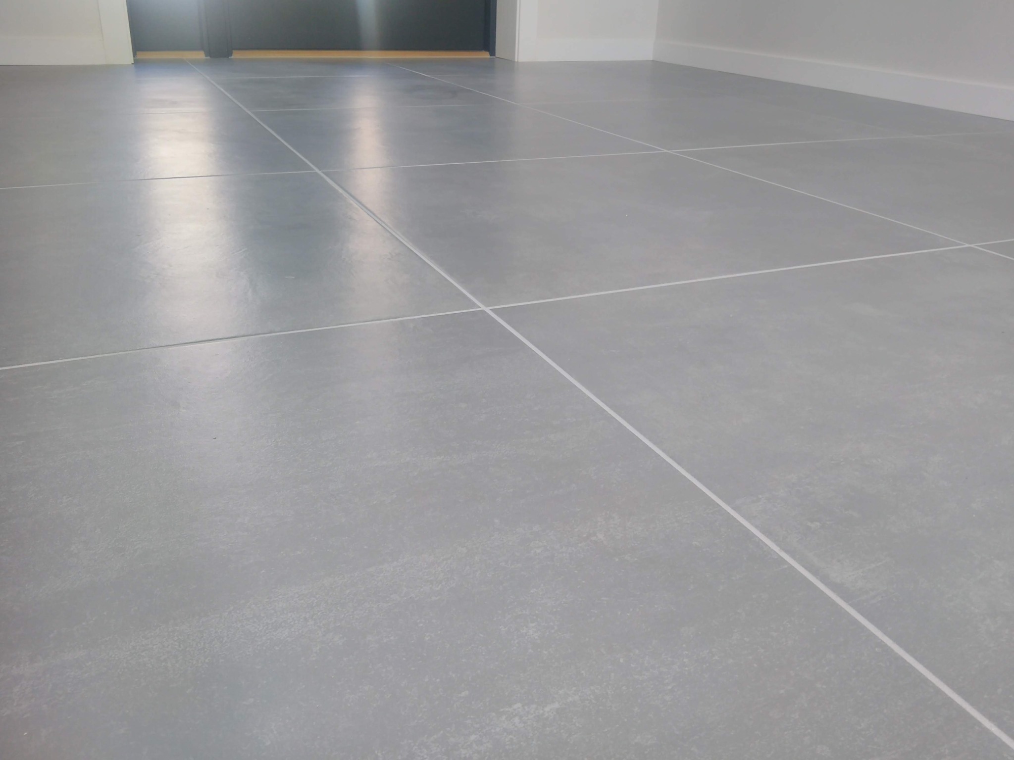 Jasnoszara podłoga z płytek o matowym wykończeniu, ułożona w kwadraty z fugami w kolorze złamanej bieli, widok z niskiej perspektywy, realizacja w Gorzowie Wielkopolskim.