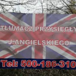 Baner reklamowy z flagą Wielkiej Brytanii i napisem 'Tłumacz przysięgły J.Angielskiego' oraz numerem telefonu, przymocowany do ogrodzenia z siatki.