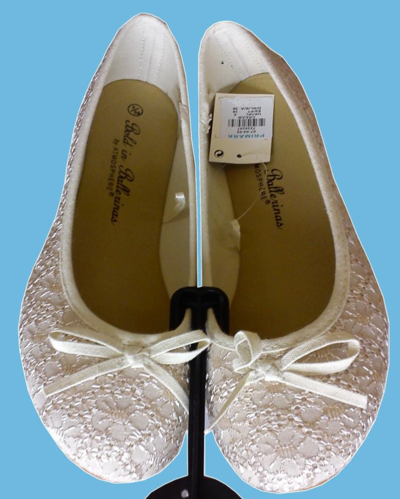 Para kremowych balerin Primark Atmosphere z koronkowym wzorem i kokardkami, prezentowanych na czarnym stojaku na tle błękitnego tła.