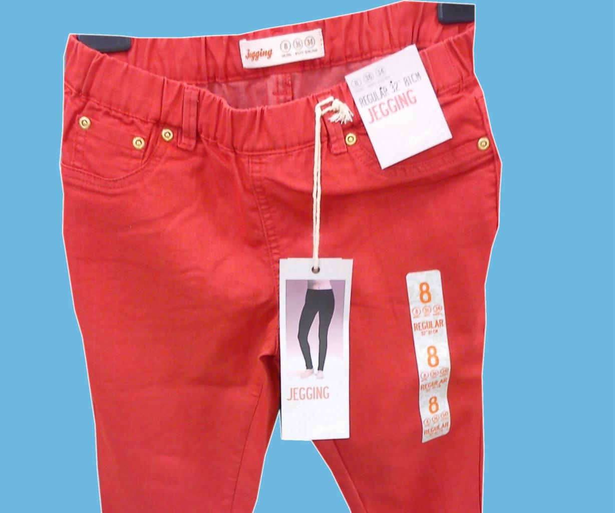 Czerwone jegginsy z metkami wiszące na wieszaku, widoczne detale: elastyczny pas, imitacje kieszeni z nitami, rozmiar 8.
