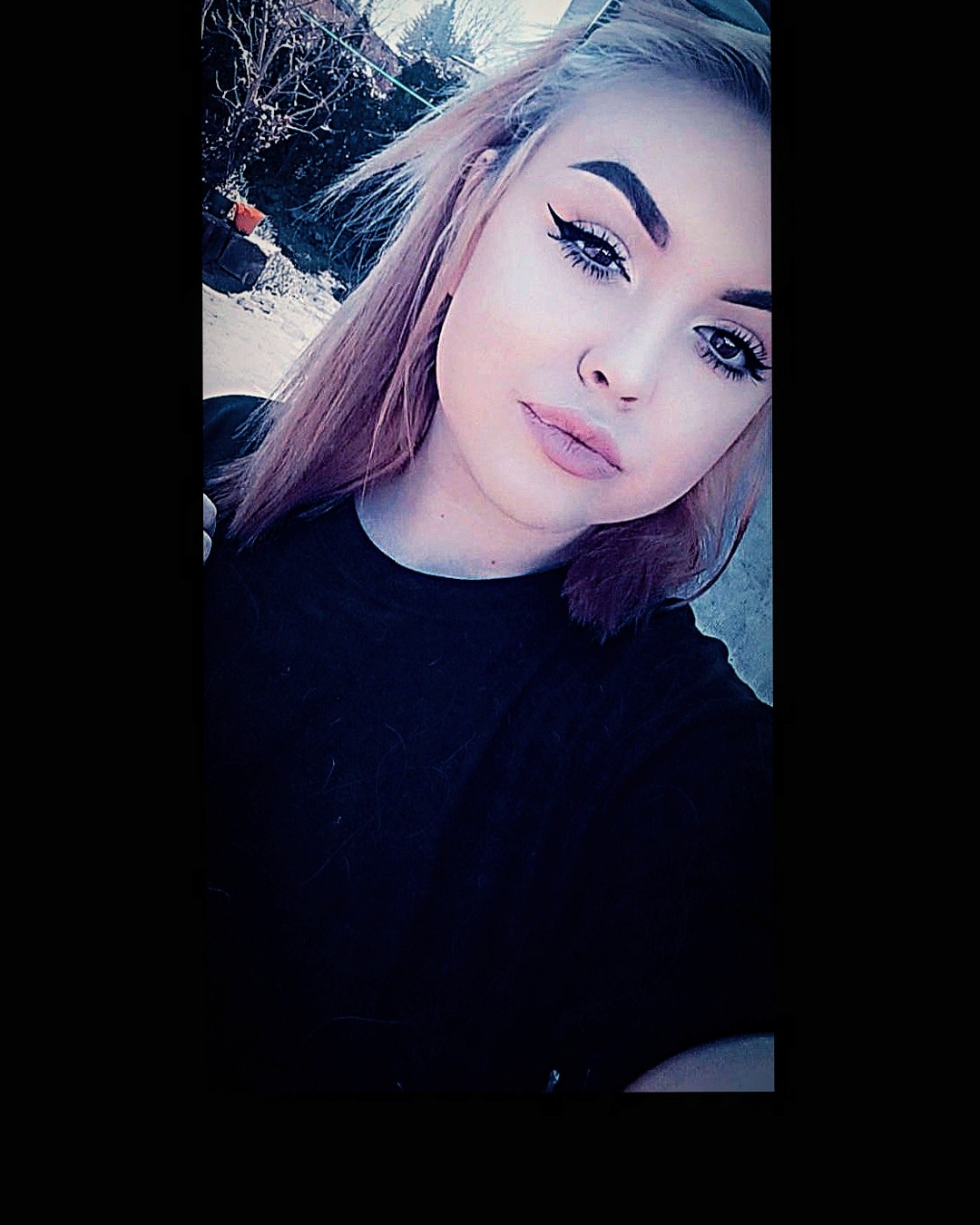 Portret młodej kobiety z delikatnym makijażem oczu i ust, z włosami w odcieniach różu, na tle rozmytego krajobrazu miejskiego.