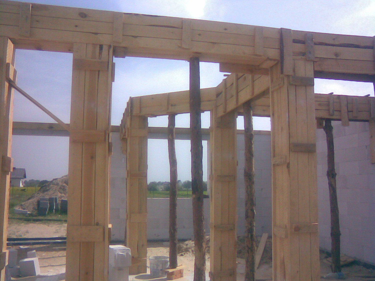 Drewniany szalunek pod budowę ścian domu z betonu komórkowego, widoczne podpory z surowych pni drzew