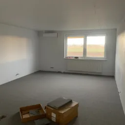 Przygotowanie do ułożenia paneli podłogowych w pustym pokoju w Józefowie, widoczne kartony z panelami i surowe ściany.