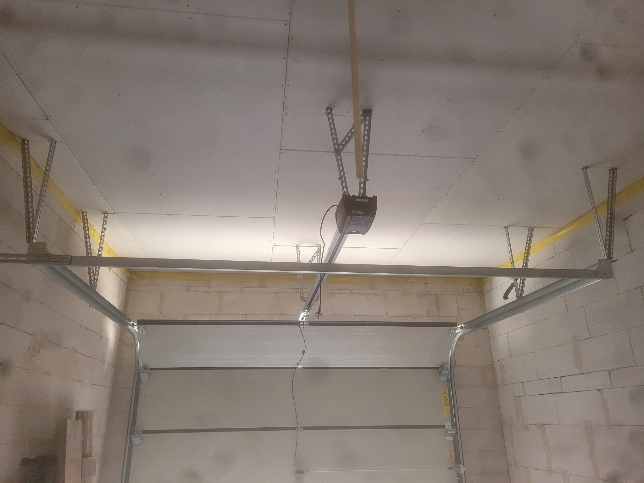 Montaż sufitu z płyt kartonowo-gipsowych w garażu z widocznym mechanizmem otwierania bramy garażowej.
