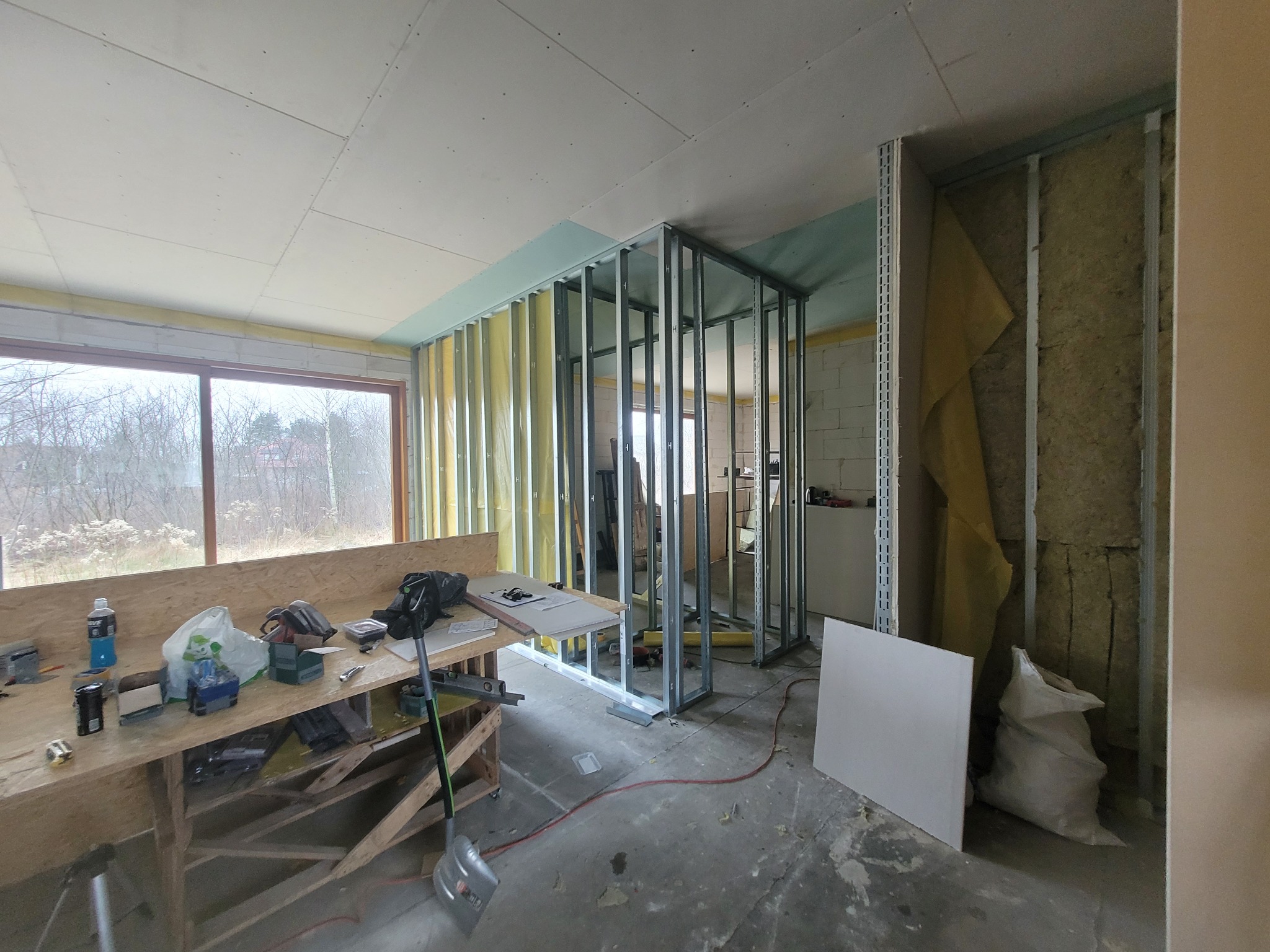 Wnętrze w trakcie prac wykończeniowych: montaż metalowej konstrukcji ścian działowych, częściowo obłożonych płytami kartonowo-gipsowymi, widoczna izolacja z wełny mineralnej, narzędzia i materiały...