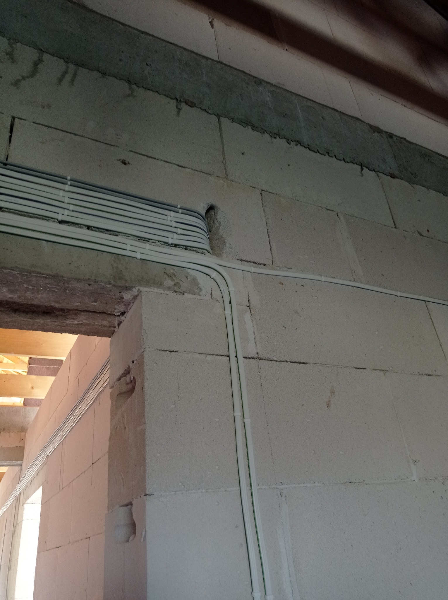 Białe przewody elektryczne ułożone w rurkach ochronnych na surowej ścianie z betonu komórkowego w trakcie budowy domu.