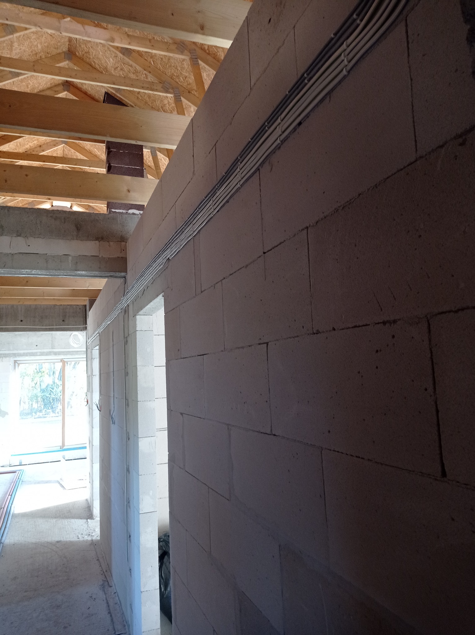 Ściana z betonu komórkowego z widocznymi przewodami elektrycznymi ułożonymi w korytkach, surowy stan budynku w trakcie budowy.