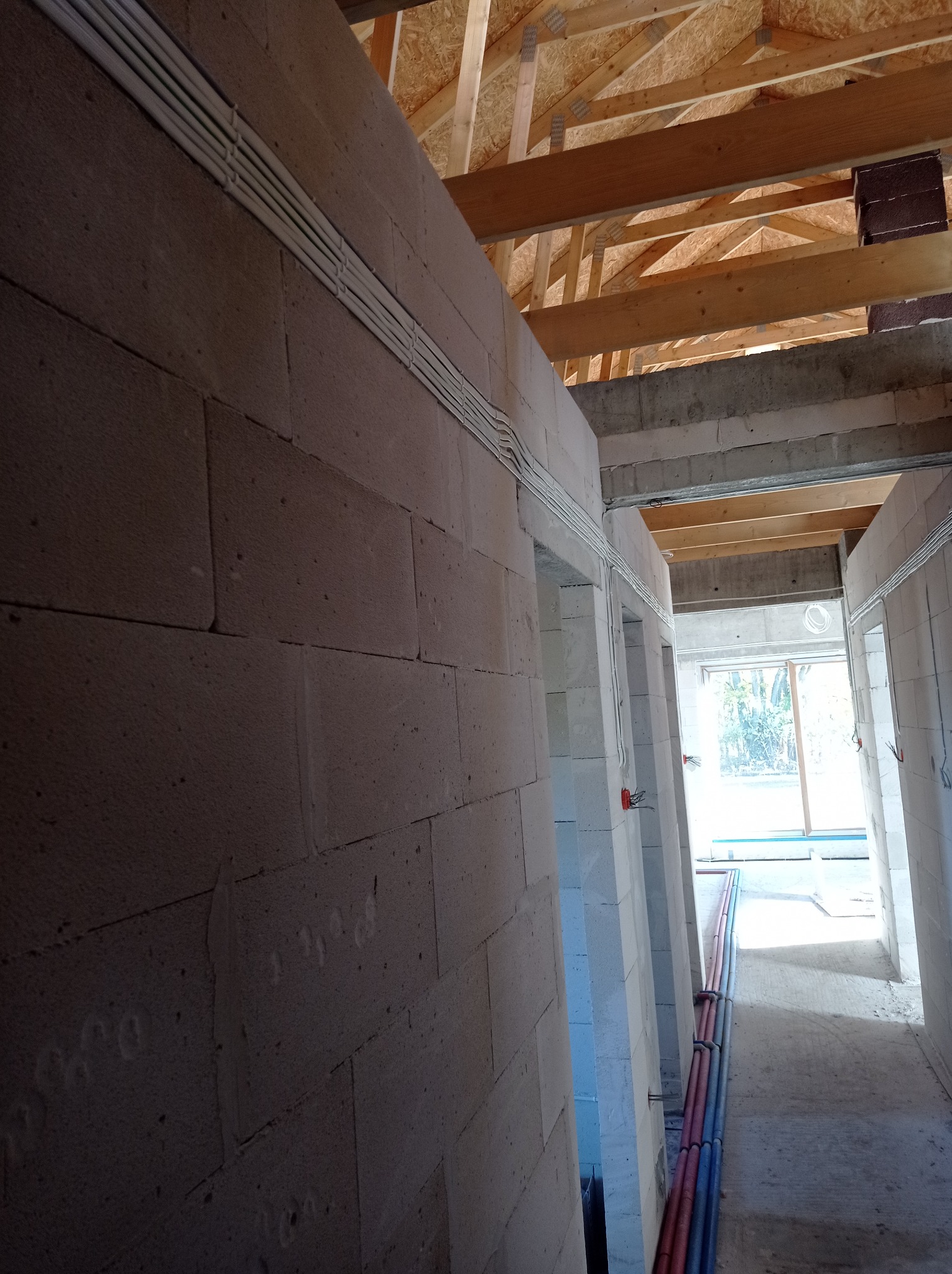 Wewnętrzne ściany budynku w trakcie budowy z widocznymi przewodami elektrycznymi ułożonymi w korytkach i rurach, surowy stan.