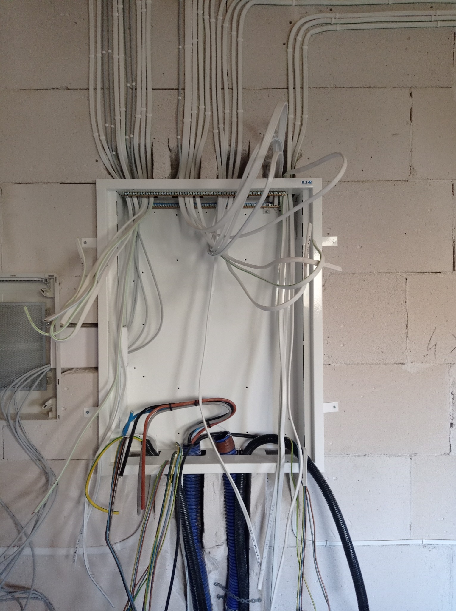 Rozdzielnica elektryczna z licznymi przewodami w białych peszlach, zamontowana na ścianie z betonu komórkowego, widoczne okablowanie w trakcie podłączania.