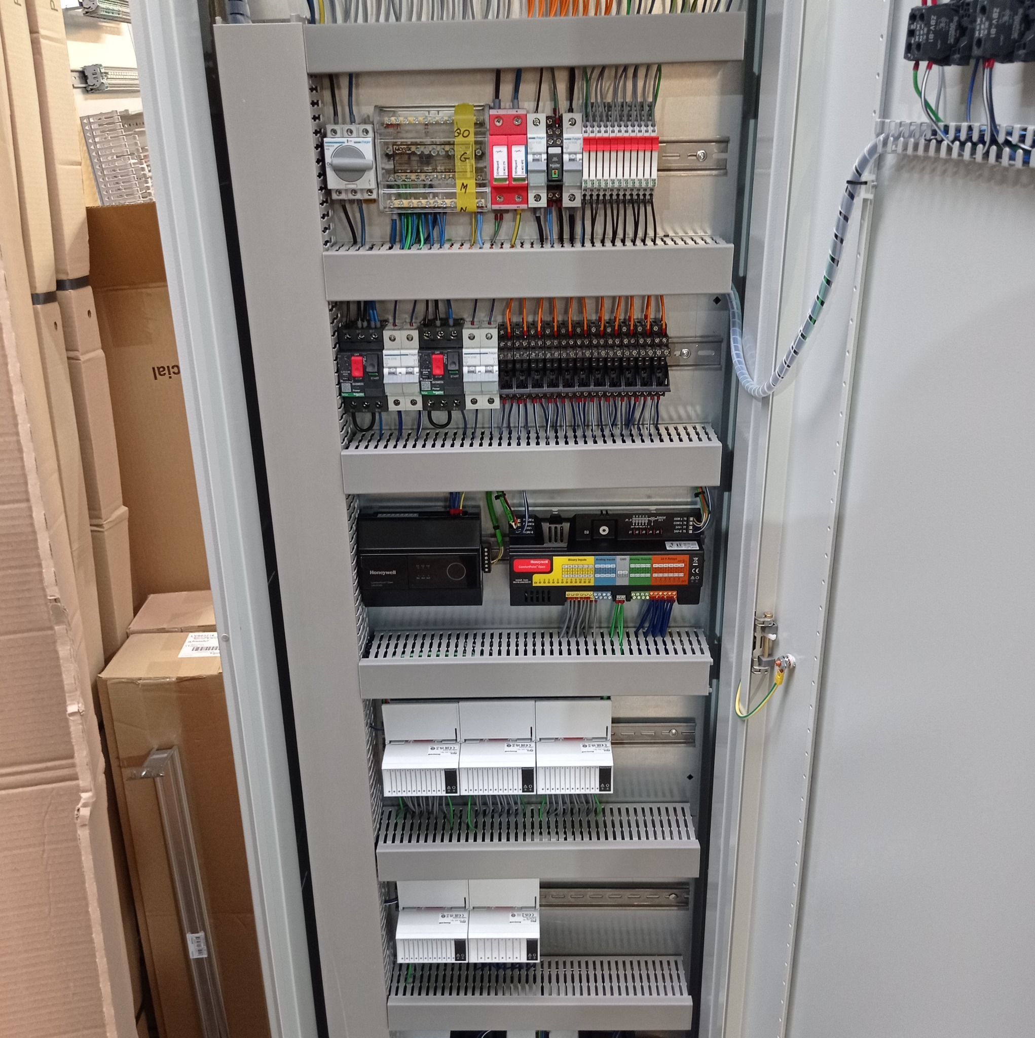 Wnętrze szafy sterowniczej z widocznymi zabezpieczeniami, modułami sterującymi Honeywell i licznymi połączeniami przewodowymi w kolorowych izolacjach.