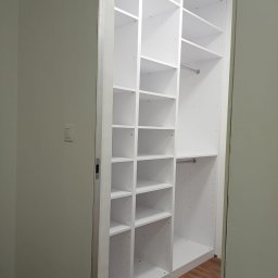 Grzegorz K - Biała, modułowa garderoba z półkami i drążkami, widoczna z perspektywy wejścia do pomieszczenia; podłoga z paneli imitujących drewno.