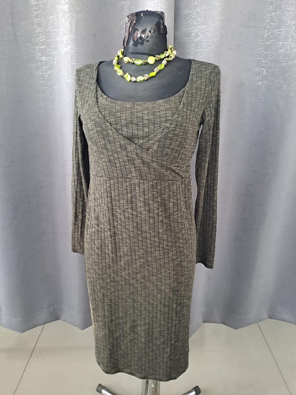 Dopasowana sukienka prążkowana w odcieniach szarości, z długim rękawem i dekoltem kopertowym, prezentowana na manekinie z zielonym naszyjnikiem z kamieni.