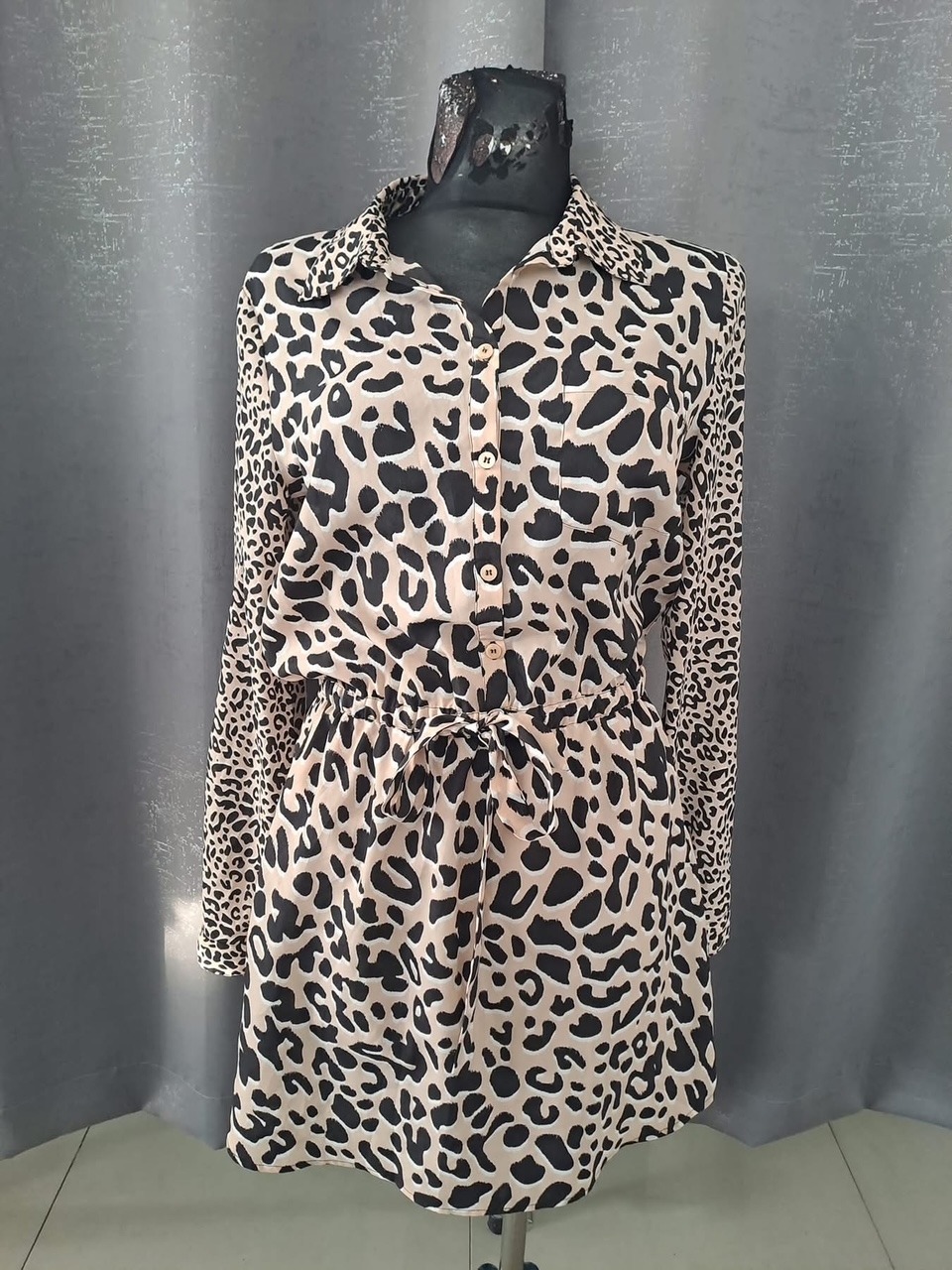 Sukienka koszulowa w panterkę z długim rękawem, przewiązana w pasie, prezentowana na manekinie na tle szarej zasłony.