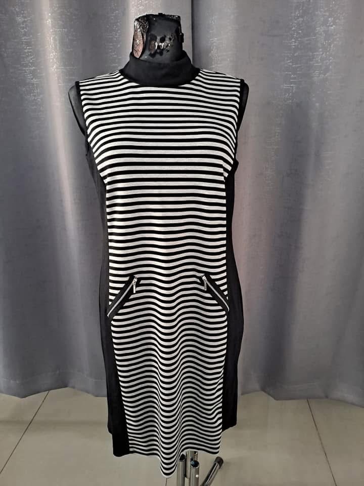 Czarno-biała sukienka w paski z ukośnymi kieszeniami na suwak, prezentowana na manekinie z dekoracyjną, metalową głową.