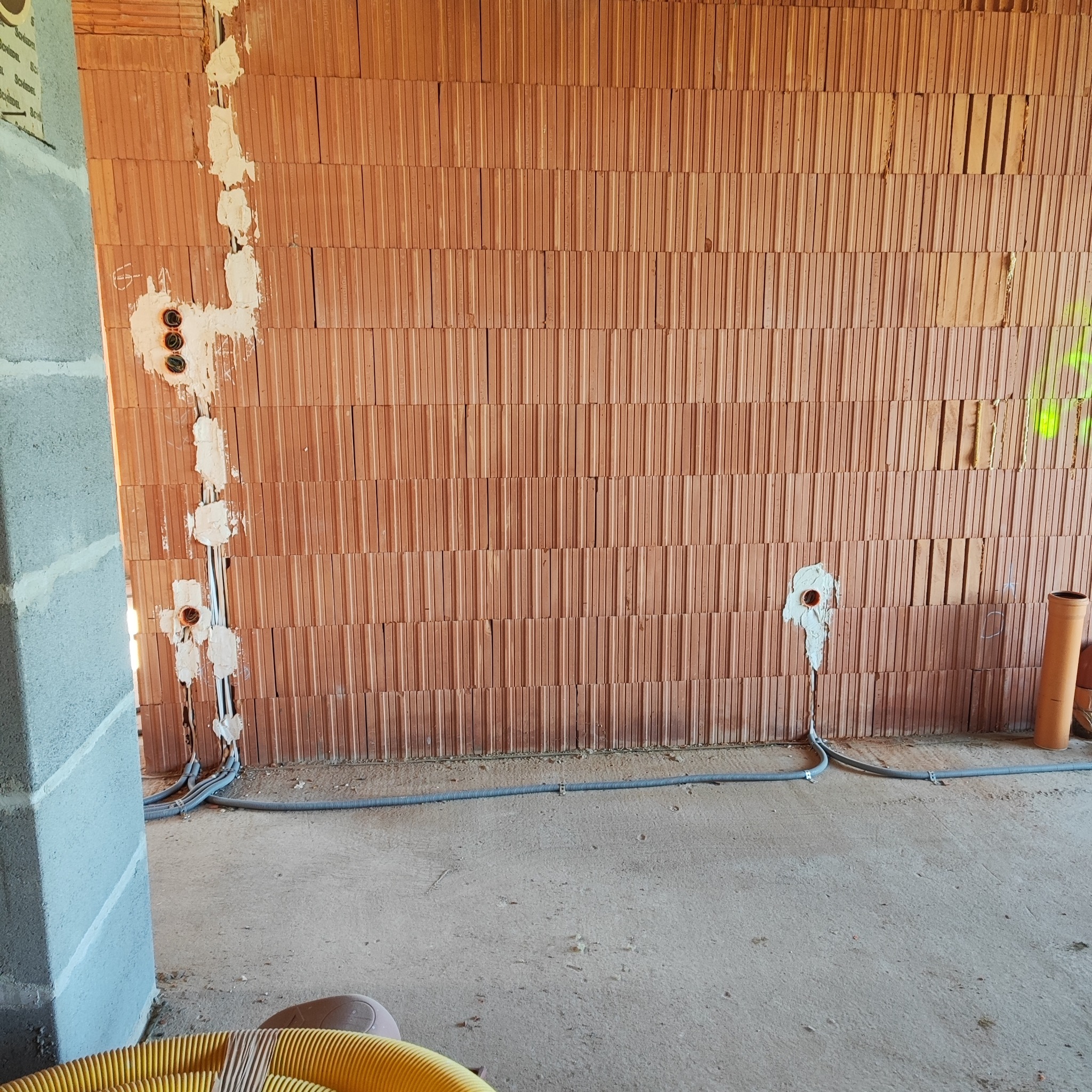 Wewnętrzna instalacja elektryczna w surowym budynku: kable w ścianie z cegły, puszki pod gniazdka zalane gipsem, rury ochronne na podłodze.