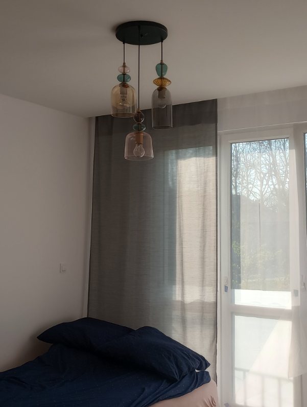 Szklana lampa wisząca z trzema kloszami w stylu vintage, zamontowana w sypialni w Rydułtowach. Dekoracyjne oświetlenie sufitowe z żarówkami.