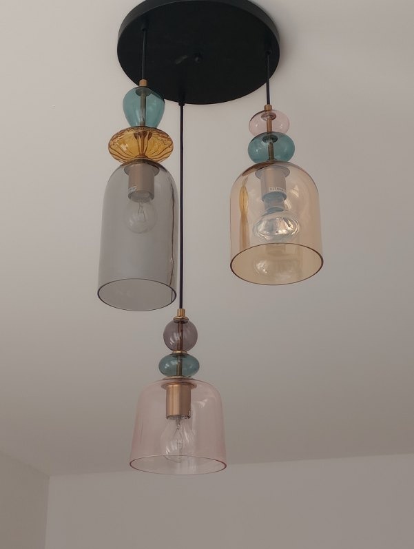 Trzypunktowa lampa wisząca z kolorowymi szklanymi kloszami w kształcie dzwonków i ozdobnymi kulami, zamontowana na czarnej, okrągłej podsufitce.