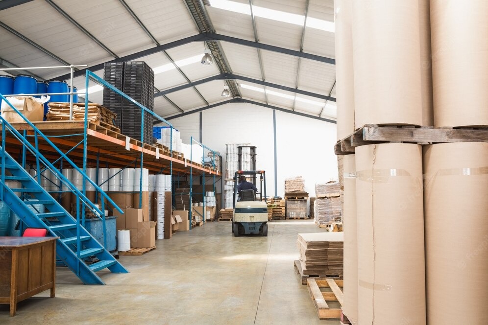 Wnętrze magazynu w Kórniku z wózkiem widłowym transportującym towary, widoczne rolki papieru i regały z zapasami.