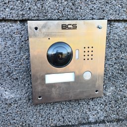 ELWAS ŁUKASZ WĄSIK - Panel domofonowy BCS z kamerą, zamontowany na szarej, chropowatej ścianie z betonu komórkowego, widoczne ślady montażu.