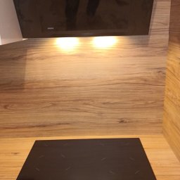 ELWAS ŁUKASZ WĄSIK - Czarna płyta indukcyjna marki Amica i okap kuchenny Akpo z naklejką 'Produkt Polski' zamontowane na drewnianym blacie.