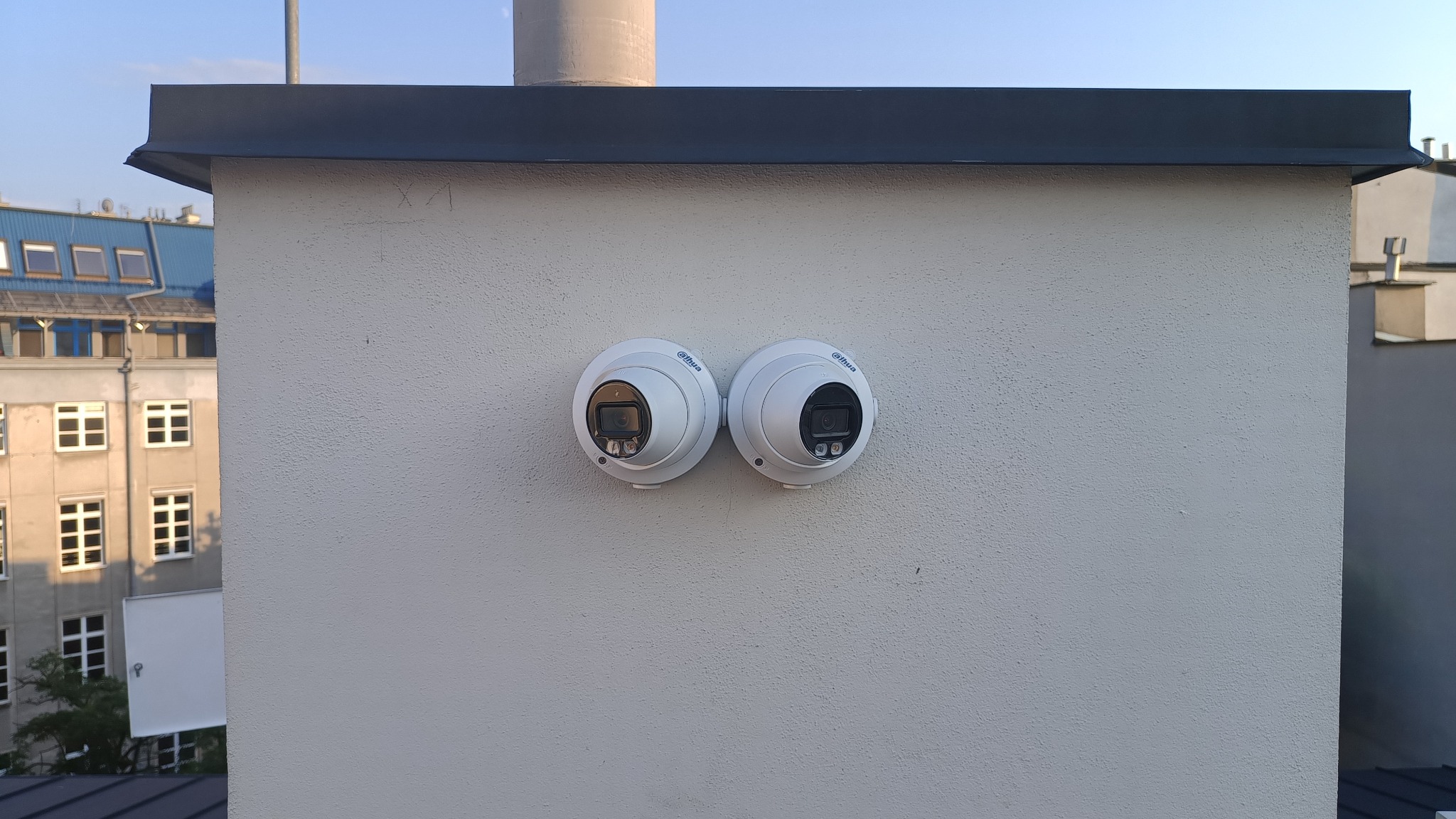 Dwie białe kamery kopułkowe marki Dahua zamontowane na szczycie komina, z widocznym budynkiem w tle.