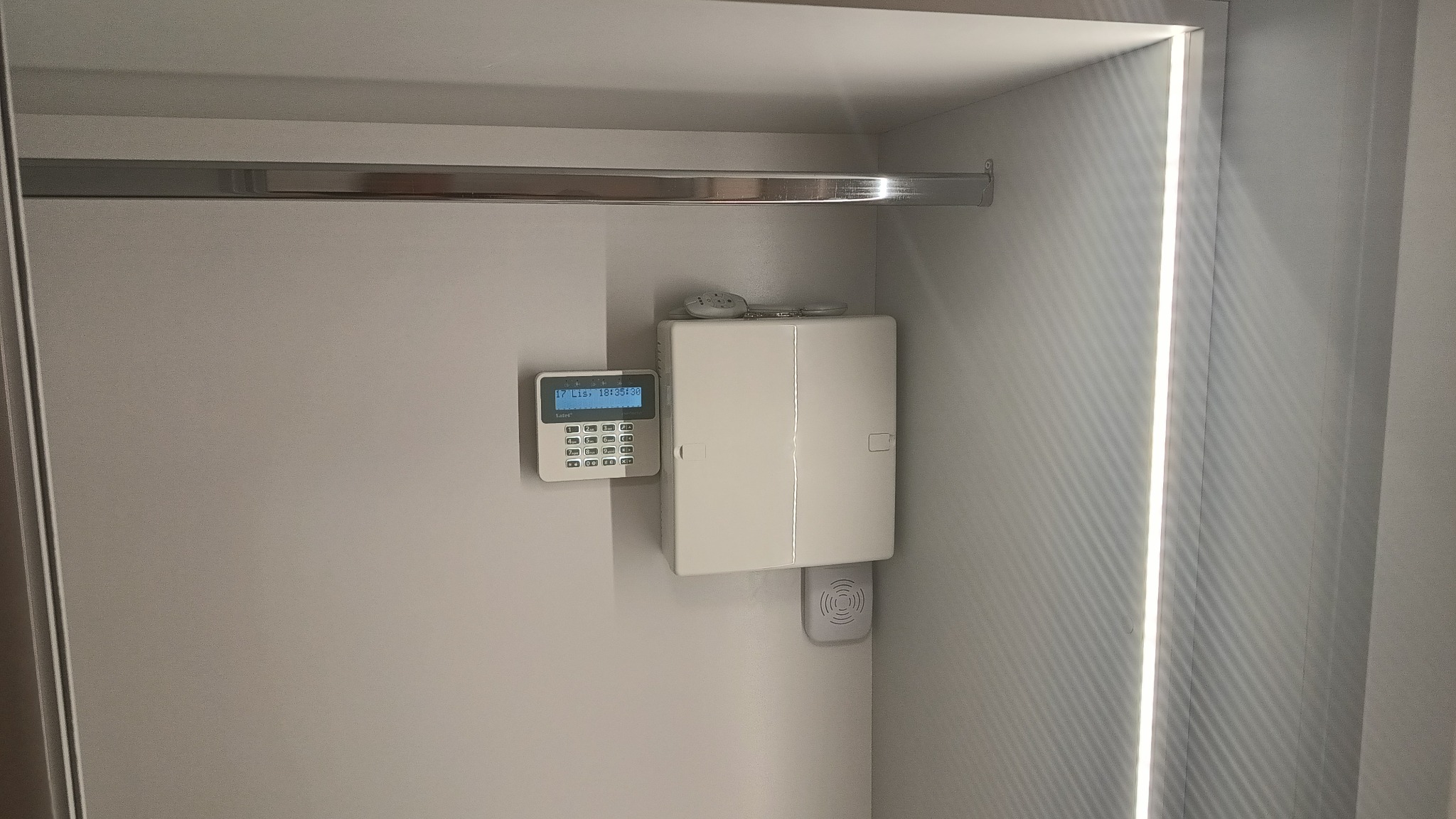 Centrala alarmowa z klawiaturą i czujnikiem, zamontowana w szafie z oświetleniem LED, widok z bliska.