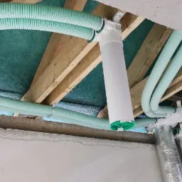 Rozprowadzenie przewodów wentylacyjnych rekuperacji pod stropem drewnianym z widocznymi elementami montażowymi i centralą w folii aluminiowej.