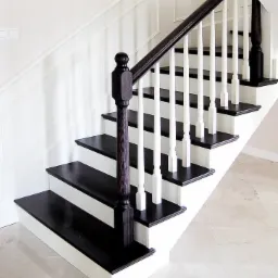 Klasyczne schody z ciemnego drewna z białymi tralkami i panelami ściennymi, widok z dołu, polerowana kamienna podłoga.