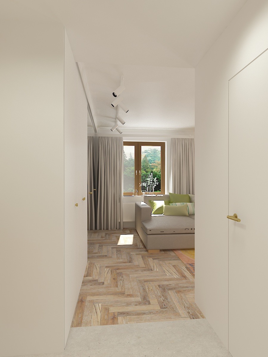 Jasne wnętrze z drewnianą podłogą ułożoną w jodełkę, beżowa sofa z zielonymi poduszkami widoczna przez otwarte drzwi, doświetlone światłem dziennym wpadającym przez okno.