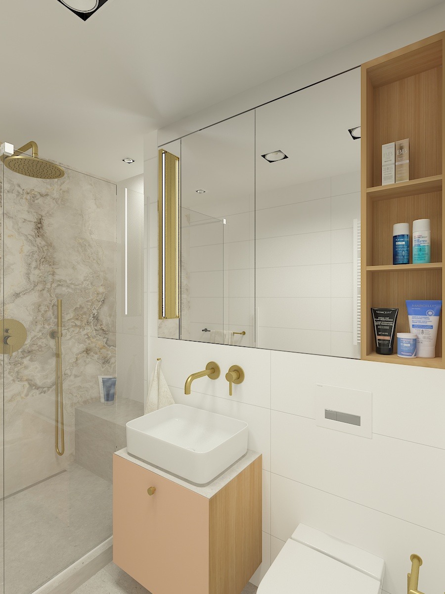 Nowoczesna łazienka z kabiną prysznicową typu walk-in, białą umywalką nablatową na szafce w odcieniach brzoskwini i drewna, oraz złotą armaturą. Na ścianie lustro w zabudowie z drewnianą półką.