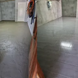 Porównanie stanu podłogi przed i po: wylewka wyrównująca w surowym stanie po lewej, ułożone szare płytki podłogowe po prawej stronie, widoczne akcesoria i narzędzia w tle.