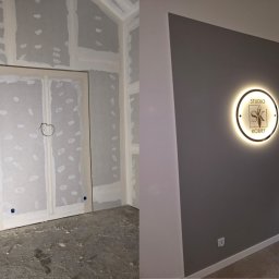 GOLD RENOVATION - Po lewej surowe ściany z płyt kartonowo-gipsowych, częściowo wyszpachlowane, z widocznymi otworami na instalacje elektryczne, po prawej pomalowana na szaro ściana z podświetlanym okrągłym logo...