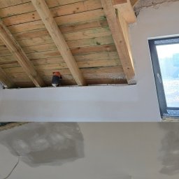 GOLD RENOVATION - Poddasze w trakcie prac wykończeniowych: drewniana konstrukcja dachu, fragment okna, ściany i sufit połatane gładzią szpachlową, widoczne ślady po wkrętach.