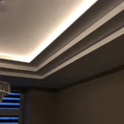 Nowoczesny sufit podwieszany z oświetleniem LED, listwy dekoracyjne i stonowana kolorystyka ścian. Widok z dołu, częściowo widoczna żaluzja okienna.