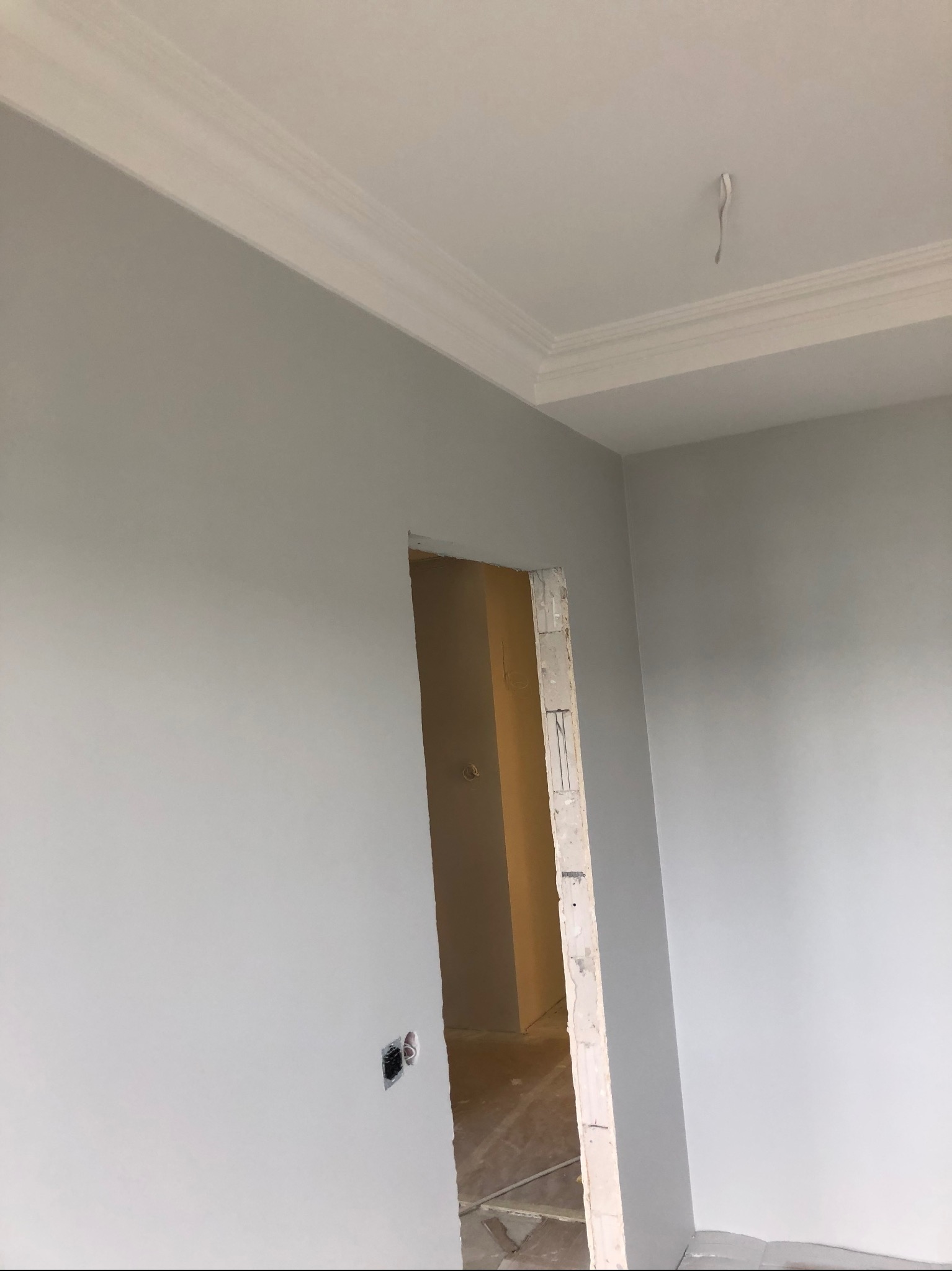 Jasnoszare ściany w świeżo wykończonym wnętrzu z dekoracyjną listwą przysufitową i widocznym otworem drzwiowym w trakcie prac wykończeniowych.