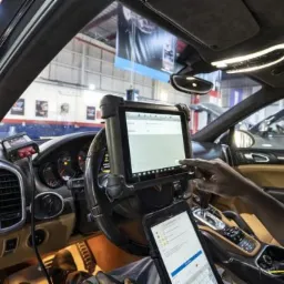 Wnętrze samochodu Porsche Cayenne, diagnostyka komputerowa za pomocą tabletu zamocowanego na kierownicy, drugi tablet w uchwycie na konsoli środkowej, widoczny kokpit i deska rozdzielcza.