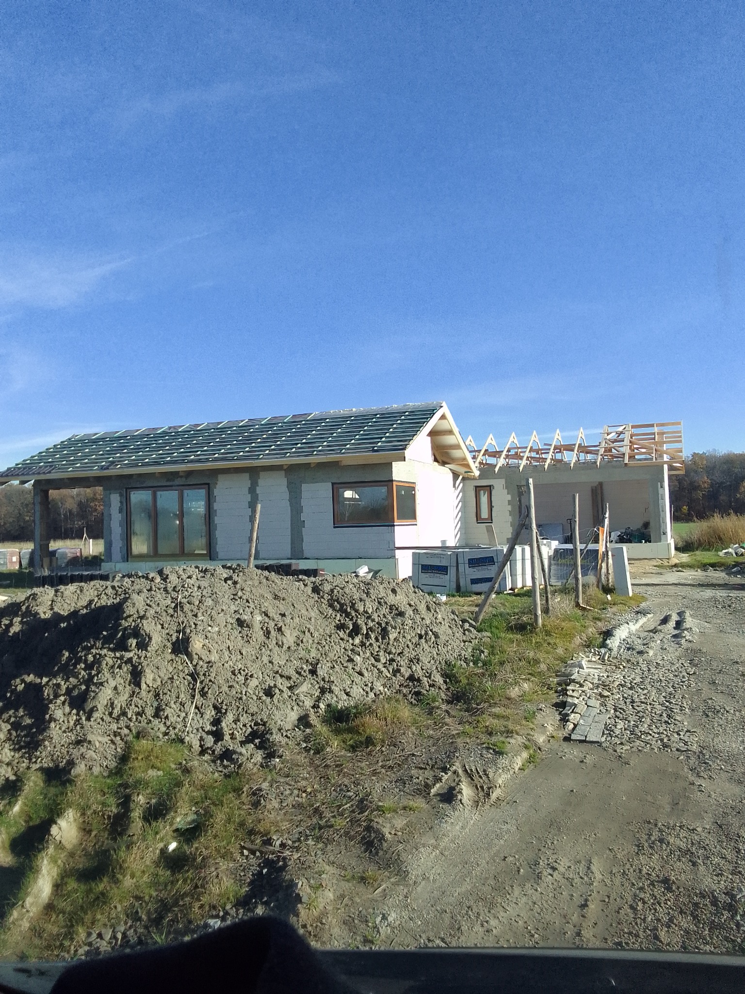 Wznoszone dwa budynki: jeden w stanie surowym zamkniętym z częściowo położoną dachówką, drugi w stanie surowym otwartym z widoczną konstrukcją więźby dachowej, na pierwszym planie hałda ziemi.